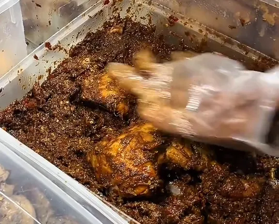 Potongan ayam direndam bumbu rempah di dalam wadah