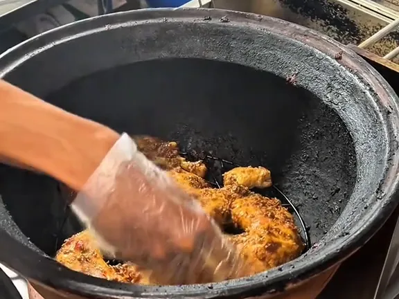 Tangan bersarung plastik menata ayam berbumbu ke dalam tungku gerabah